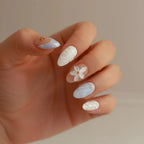 Ocean Bloom Handmade Press-On Nails close-up — short almond shape, nude base with lavender-blue diagonal marble and gold starfish charm on thumb, white 5-petal flower on middle finger, light blue aurora texture on ring finger, pearl dot pinky | MOONLEE