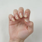 Close-up of hand wearing Golden Hour handmade press-on nails — light skin tone, short oval champagne nude pearl nails, index finger with tiny silver bead constellation decoration, elegant and minimal, soft white background
