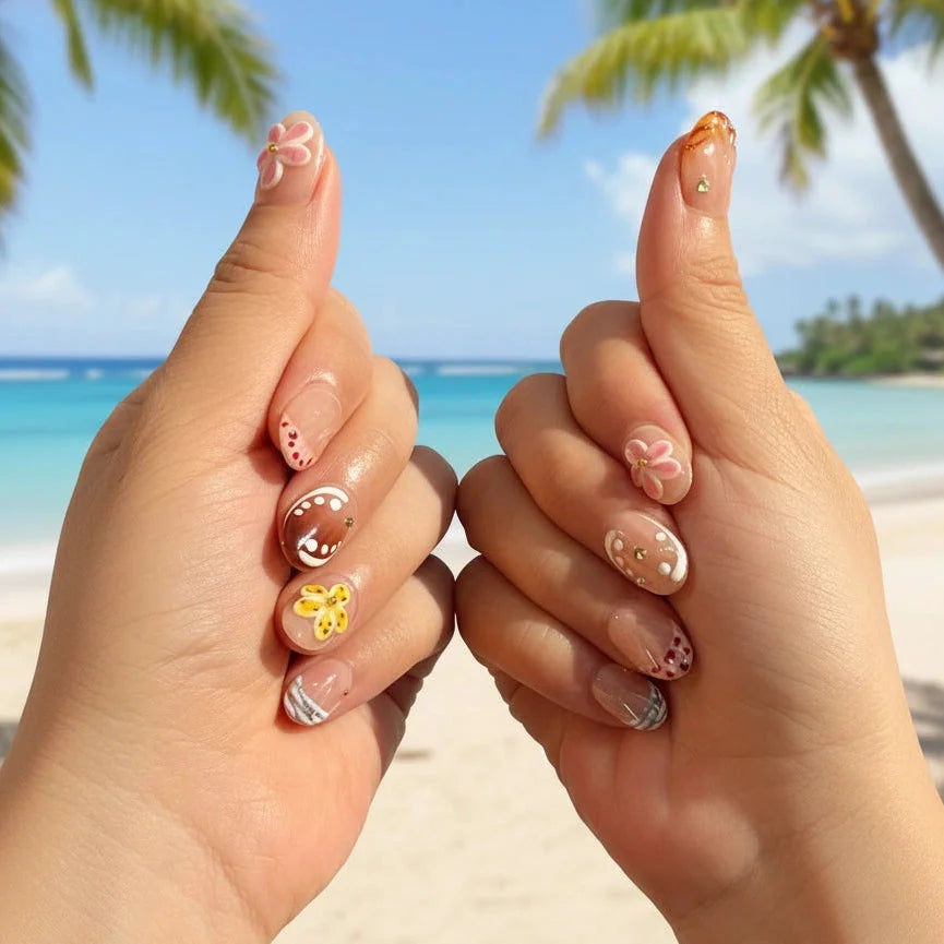 Whispering Sands Handmade Press-On Nails — both hands with short round nails featuring pink cherry blossom flower, brown gradient with pearl dots and gold rhinestone, yellow starfish with gold center, burgundy red dot clusters, purple-blue watercolor stripes, Hawaii tropical beach background | MOONLEE